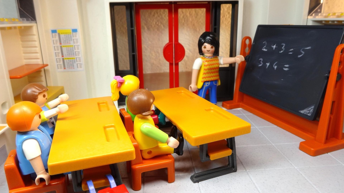 Zu sehen ist ein Playmobilklassenzimmer mit vier Kindern an Schultischen und einer Lehrerin vorne an der Tafel. © Pixaby