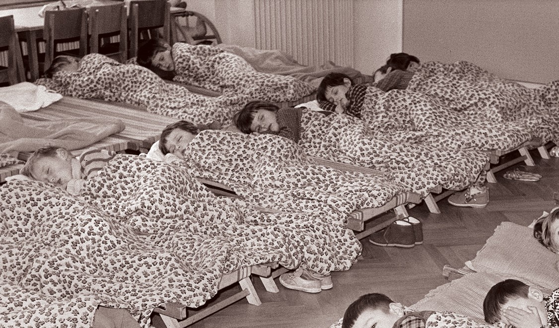 In Reihen stehen dicht gedrängt Betten, darin liegt je ein Kind und schläft. Die Kinder sind zugedeckt.  © Wikimedia