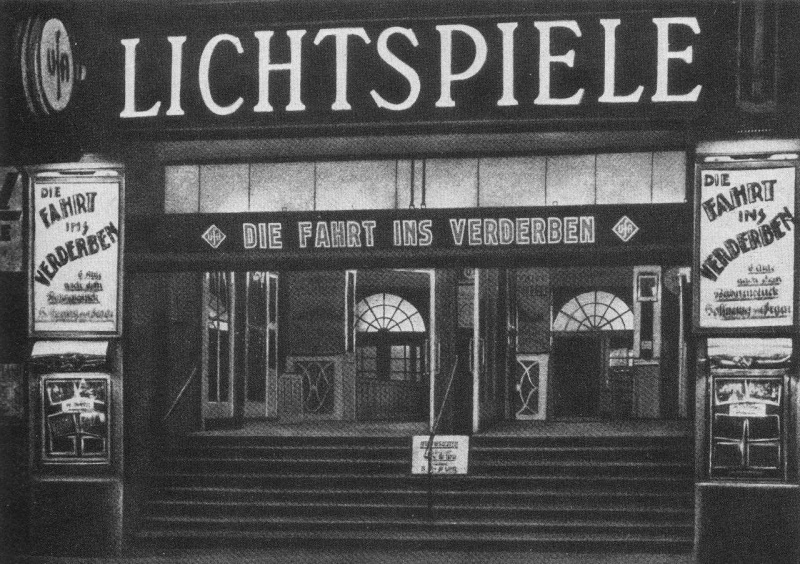 Am Eingang eines Kinos wird der Film „Die Fahrt ins Verderben“ beworben. Auf einem Schild steht groß „Lichtspiele“. Treppen führen hinauf in den Innenraum des Kinos. Links und rechts der Treppe hängen Filmplakate für den beworbenen Film.  © wikimedia