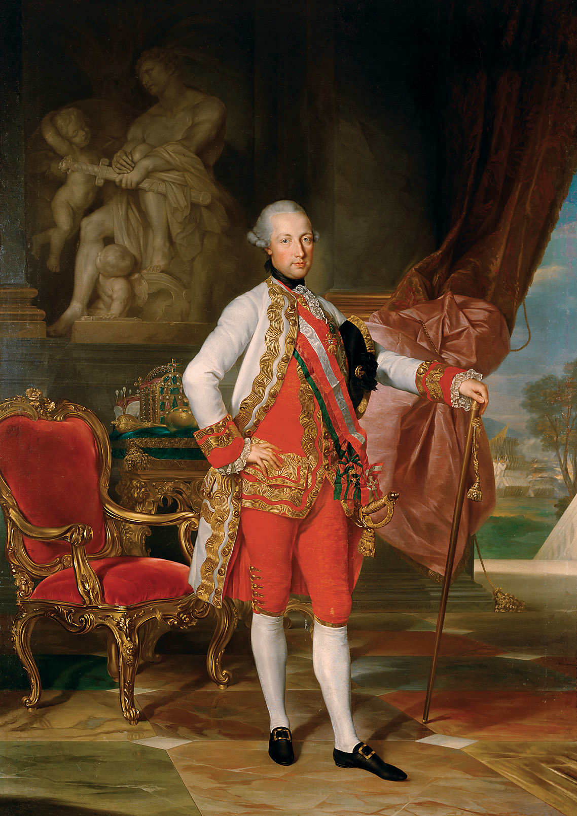 Joseph II. steht in prächtigem Gewand in einem Prunksaal. Er trägt einen weißen Mantel mit goldenen Verzierungen, darunter rote Kleidung und eine rot-weiß-rote Scherpe. Auf dem Kopf hat er eine silbergraue Perücke.  © Wikimedia. 