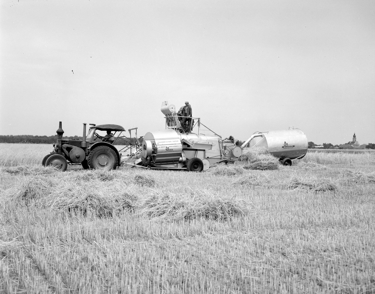 Ein Traktor bei der Getreideernte zieht eine lange Erntemaschine hinter sich her, auf der eine Person steht. © ÖNB Bildarchiv