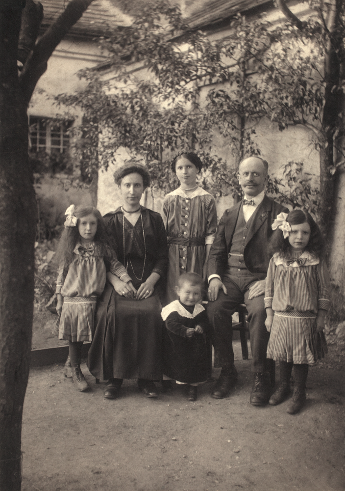 Familienporträt der Familie Biegler in einem Garten. Zu sehen sind alle sechs Familienmitglieder und dahinter ein Haus. Die Eltern sitzen auf Sesseln. Die Kinder stehen daneben.  © Foto in Besitz von Friedrich Polleroß