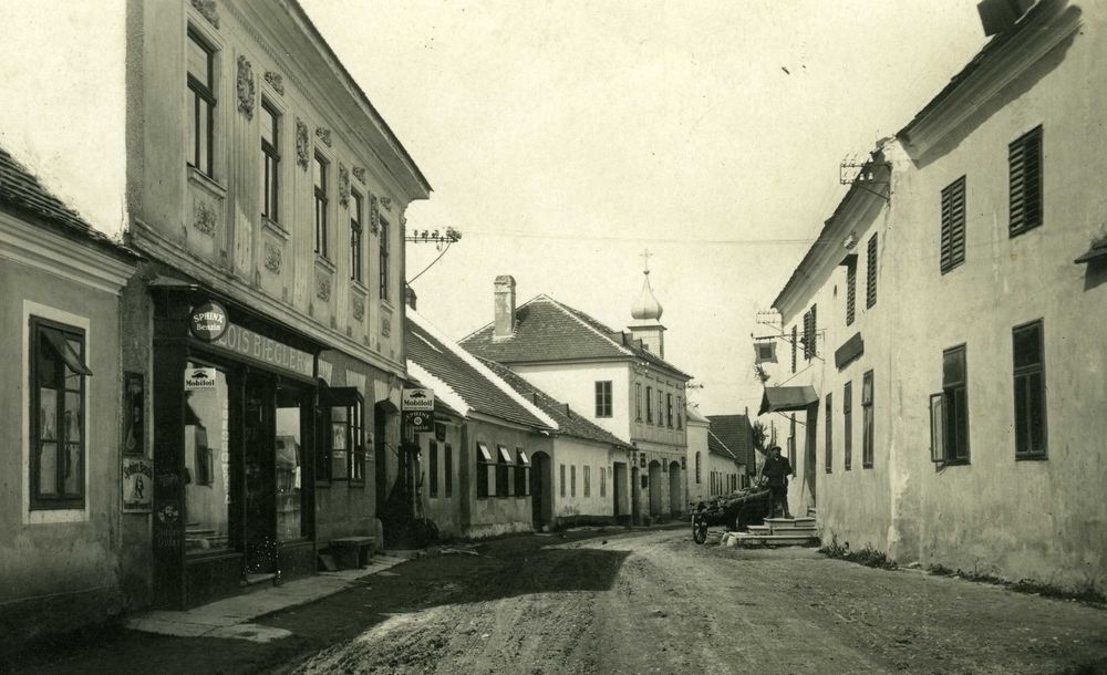 Eine Dorfstraße mit Häusern links und rechts. Am zweiten Haus von links steht auf einem Schild „Alois Biegler”. Weiter hinten auf der rechten Seite der Straße steht ein Mann. © 1935, im Besitz von Friedrich Polleroß