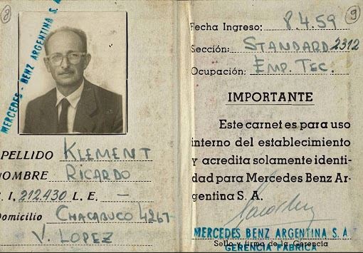 Der Ausweis aus gelblichem Papier mit schwarzer Druckschrift zeigt ein Foto von Adolf Eichmann in Anzug und Krawatte und mit Brille. Der Name und die anderen Daten seiner gefälschten Identität sind in blauer Tinte eingetragen. Auf dem Ausweis befinden sich zwei blaue Stempel von Mercedes Benz Argentinien.  © Wikimedia, Eichmanns gefälschter Ausweis auf den Namen Ricardo Klement. 