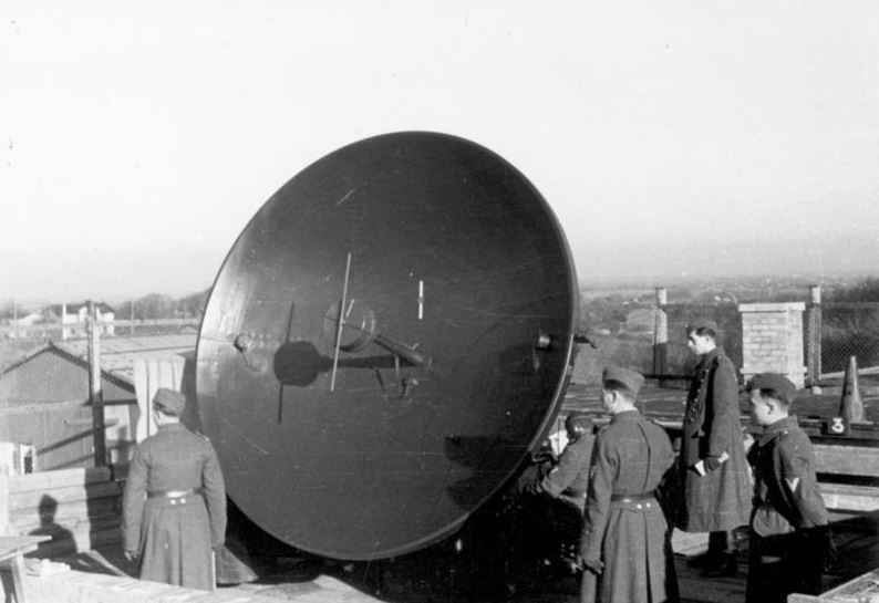 Soldaten stehen um ein Radargerät herum. Das Gerät hat die Form einer riesigen Schüssel, die in Richtung des Fotografen geneigt ist.  © Wikimedia, Bundesarchiv, Bild 101I-621-2930-32/Walther, Telefunken-Radargerät „Würzburg“ im Einsatz bei der Wehrmacht, 1942, CC-BY-SA 3.0. 