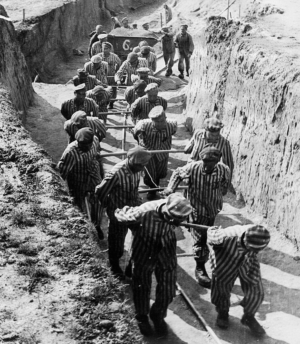 Das Schwarz-Wei&szlig;-Foto zeigt einige H&auml;ftlinge, die in einem Graben einen Wagen mit Erde ziehen. Die H&auml;ftlinge tragen gestreifte Kleidung und M&uuml;tzen.&nbsp; &copy; United States Holocaust Memorial Museum, H&auml;ftlinge ziehen eine Lore beim Bau des sogenannten Sanit&auml;tslagers im KZ Mauthausen, Sommer 1942, gezeigt bei Boix&lsquo; Zeugenaussage in N&uuml;rnberg, Signatur: 12352. 