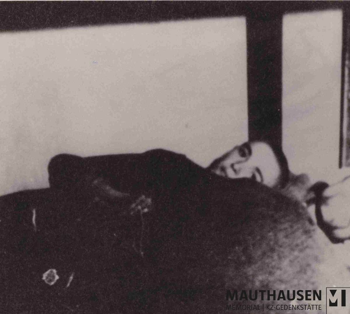 Das Schwarz-Wei&szlig;-Foto zeigt zwei befreite H&auml;ftlinge, die geschw&auml;cht nebeneinander im Stockbett liegen. Hinten liegt ein junger Mann mit kurzem Haar, der hinter einer dunklen Decke hervor in die Kamera schaut. Vom Mann im Vordergrund ist nur das Kinn erkennbar. &copy; Mauthausen Memorial, Sammlung Hans Mar&scaron;&aacute;lek, &Uuml;berlebende im Stockbett im befreiten KZ Gusen, Mai/Juni 1945, Signatur: 4.1.0303, Ausschnitt.