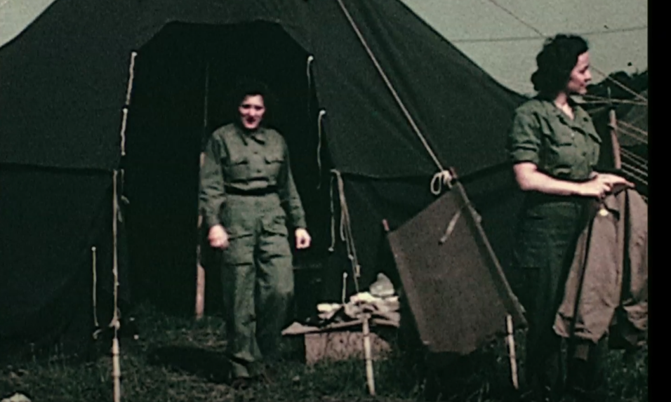 Der Videoscreenshot zeigt ein Zelt eines mobilen US-Spitals. Der Zelteingang ist offen, davor steht eine Krankenschwester in dunkelgr&uuml;ner Milit&auml;runiform und schaut in die Kamera. Rechts im Bild befindet sich eine zweite Krankenschwester in Uniform. Das Zelt ist mit Seilen befestigt. &copy; United States Holocaust Memorial Museum, Krankenschwestern des 51st Field Hospital der US-Armee, Frankreich 1944, Signatur: RG-60.1397, Videoscreenshot 46&rsquo;&rsquo;.