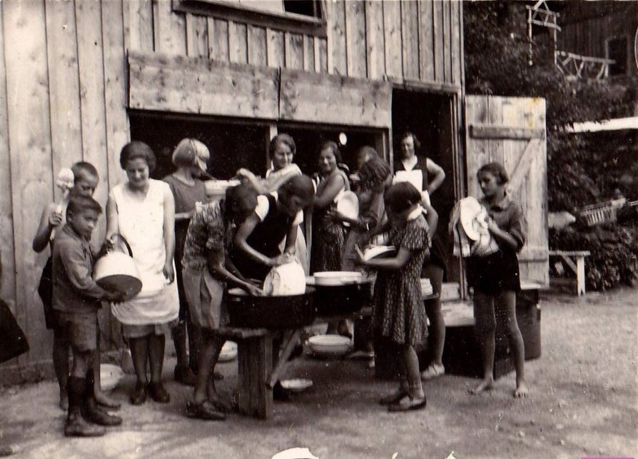 Frauen und Kinder stehen um einen Tisch vor einer Hütte, wo gekocht und abgewaschen wird. © Archiv SPÖ