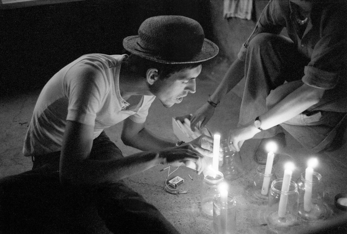 Ein Mann mit Hut stellt Kerzen in Einmachgläser und zündet sie mit Streichhölzern an.  © Heinz Riedler, Wien Museum.