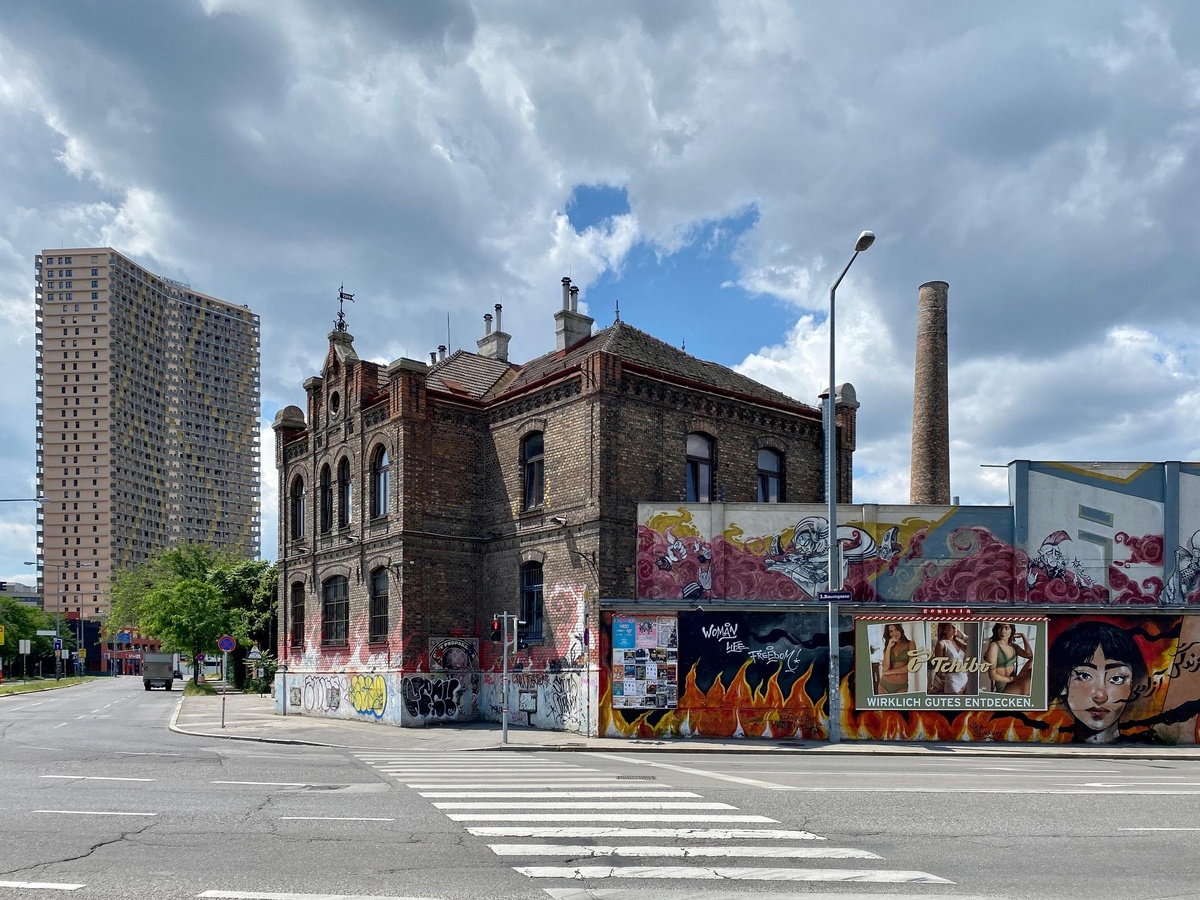 Im Vordergrund steht das Arena-Gebäude aus Backstein. Die Wände sind mit Graffiti besprüht. Im Hintergrund steht ein neues Hochhaus.  © Q-Tower Arena, Funke, Wikimedia, CC-BY-SA-4.0.