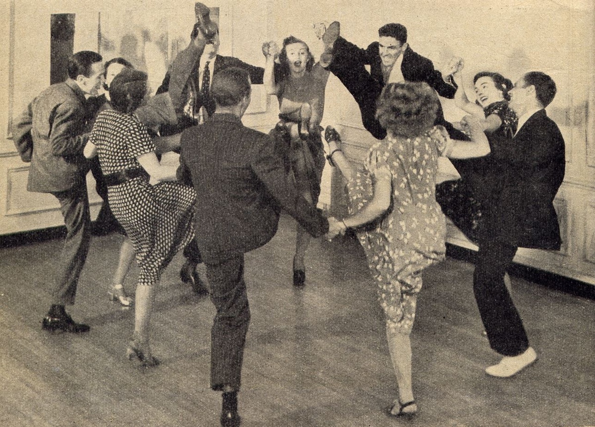 Jugendliche in Kleidern und Anzug bewegen sich in einem Zimmer mit Parkettboden im Kreis, halten sich an den Händen und tanzen, indem sie ein Bein hoch in die Luft werfen.  © DAS MAGAZIN,Nr. 171, 1938 - Original im Barmbeker Schallarchiv
