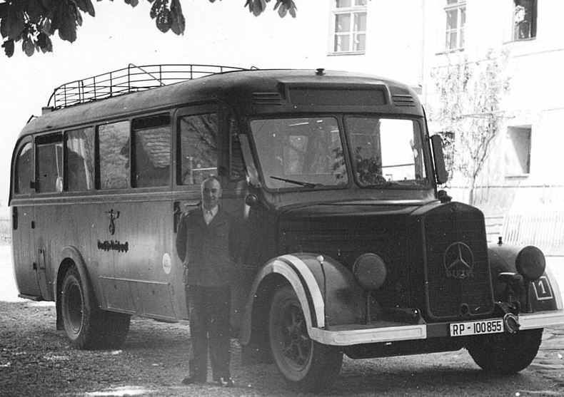 Ein Mann steht vor einem dunkel lackierten Bus. Im Hintergrund befinden sich die hellen Mauern des Schlosses mit Fenstern.  © Wikimedia, Bus vor der NS-Tötungsanstalt Hartheim, um 1940, CC-BY-SA-3.0-migrated-with-disclaimers