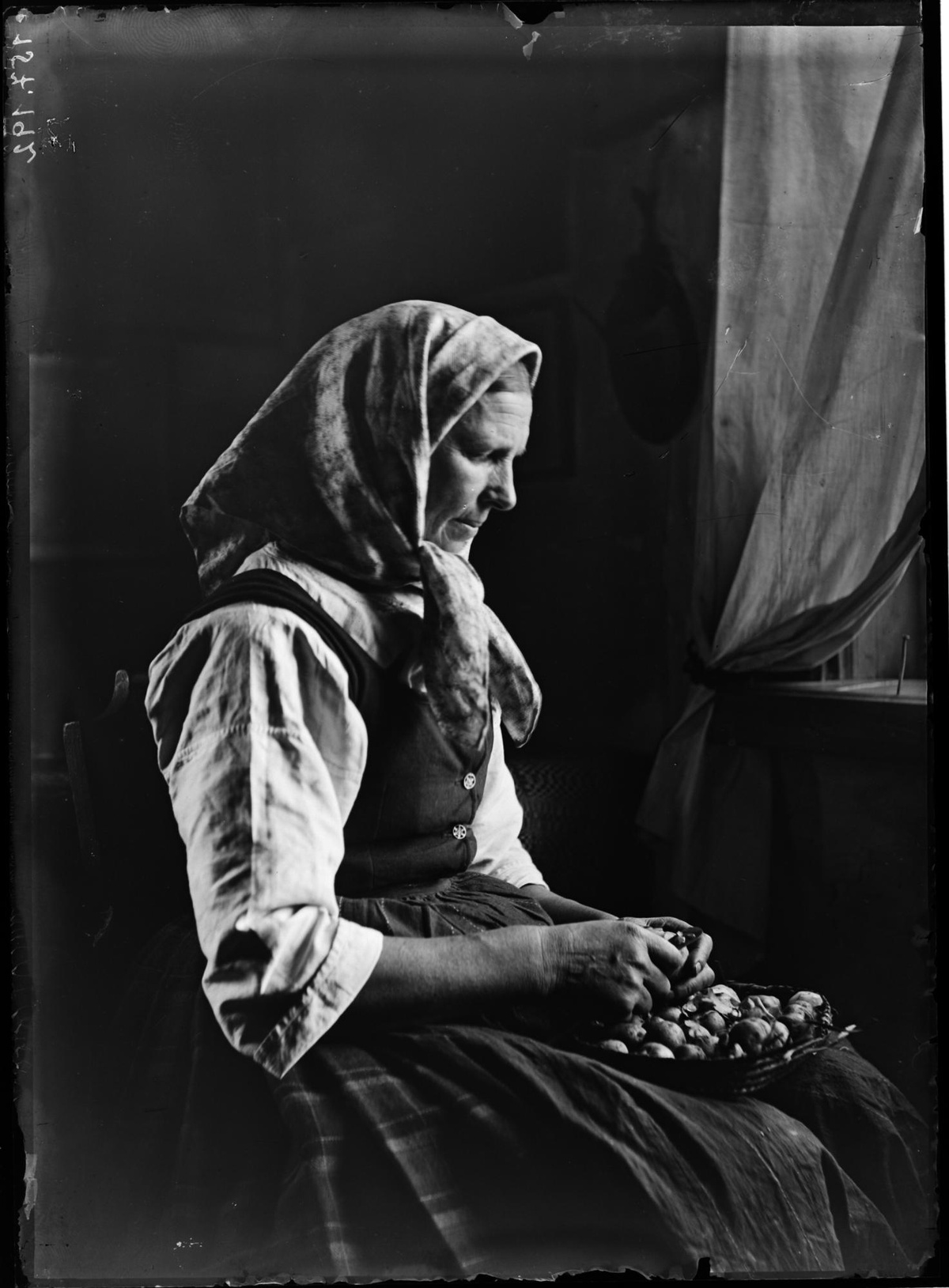 Portrait einer Frau aus dem Jahr 1895 beim Erdäpfelschälen. Sie sitzt am Fenster, durch das Licht in den Raum fällt. © ÖNB
