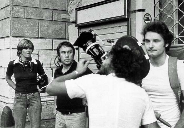 Das Schwarzwei&szlig;foto zeigt einen Mann mit einer gro&szlig;en Filmkamera &uuml;ber der Schulter. Rundherum stehen zwei M&auml;nner und eine Frau und schauen zu. &copy; Elisabeth Guggenberger und Helmut Voitl bei Drehbeginn