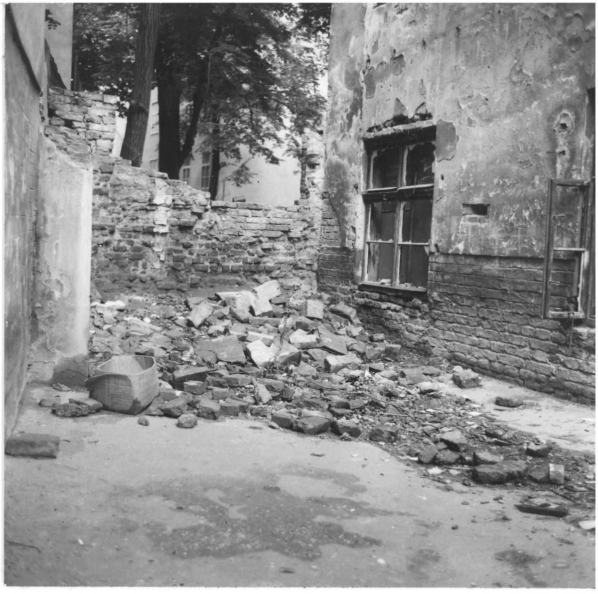 Das Schwarzwei&szlig;foto zeigt eine sch&auml;bige Fassade und davor eine verfallende Mauer. Vor der Mauer liegt ein gro&szlig;er Haufen Schutt.  &copy; Gartenhofverein Planquadrat, Innenhof