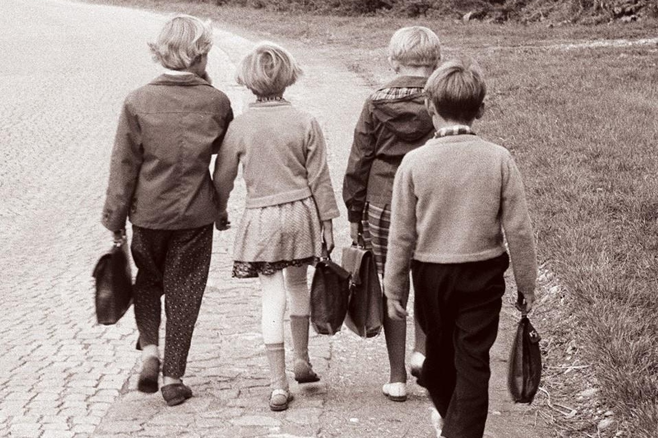 Vier Kinder gehen am Straßenrand entlang, jedes hat eine Tasche in der Hand.  © Wikimedia. 