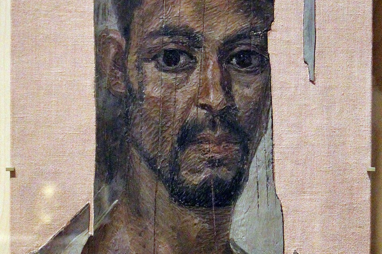 Porträt eines Mannes mit dunklen Haaren, Augen und Bart und weißer Kleidung. © Wikimedia, Mumienporträt. 