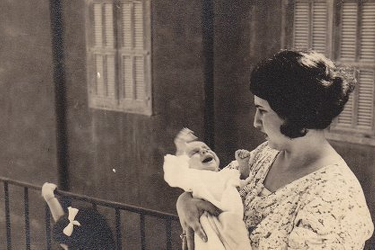 Eine Mutter mit dunklen Haaren und angespanntem Gesichtsausdruck hält ein Baby im Arm. Das Baby schreit und strampelt. Links neben der Frau ist der Kopf eines Mädchens mit weißer Schleife im Haar zu sehen.  © Wikimedia, Mutter mit Baby, 1935. 