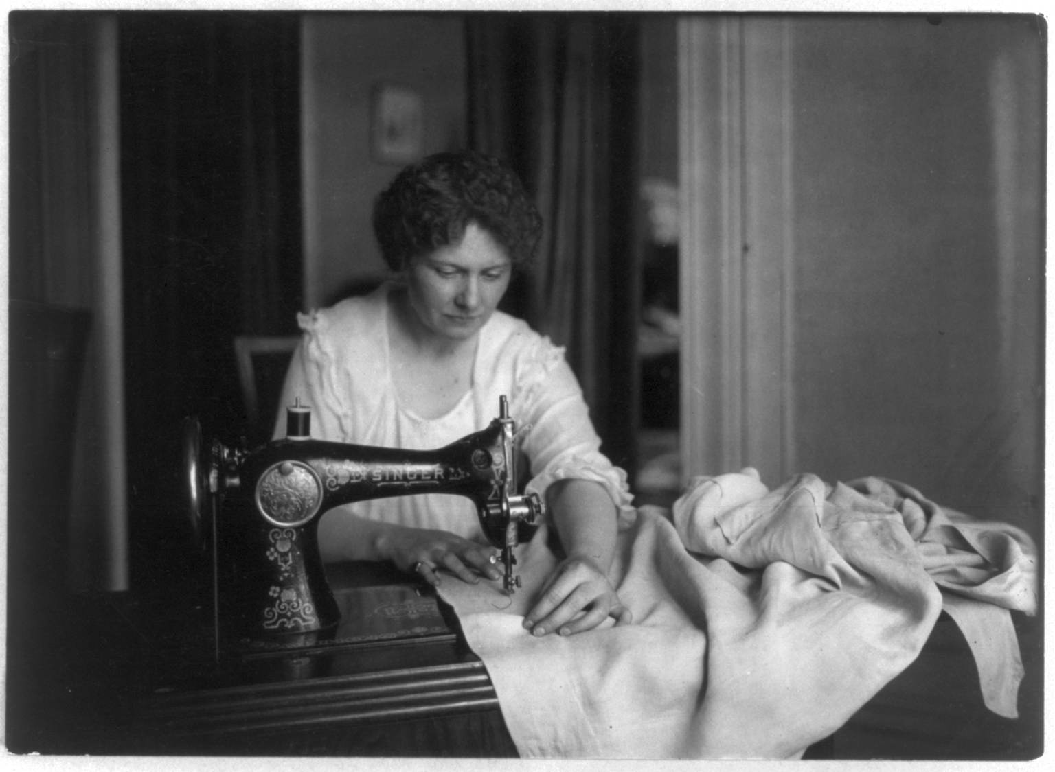 Eine Frau sitzt an einer Singer-Nähmaschine und näht.  © Wikimedia. 