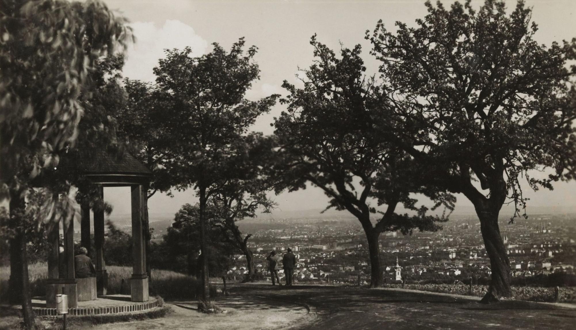 Ein Pavillon, Bäume und zwei Menschen auf einer Aussichtsplattform mit Blick auf die dahinterliegende Stadt Wien.  © Wien Museum
