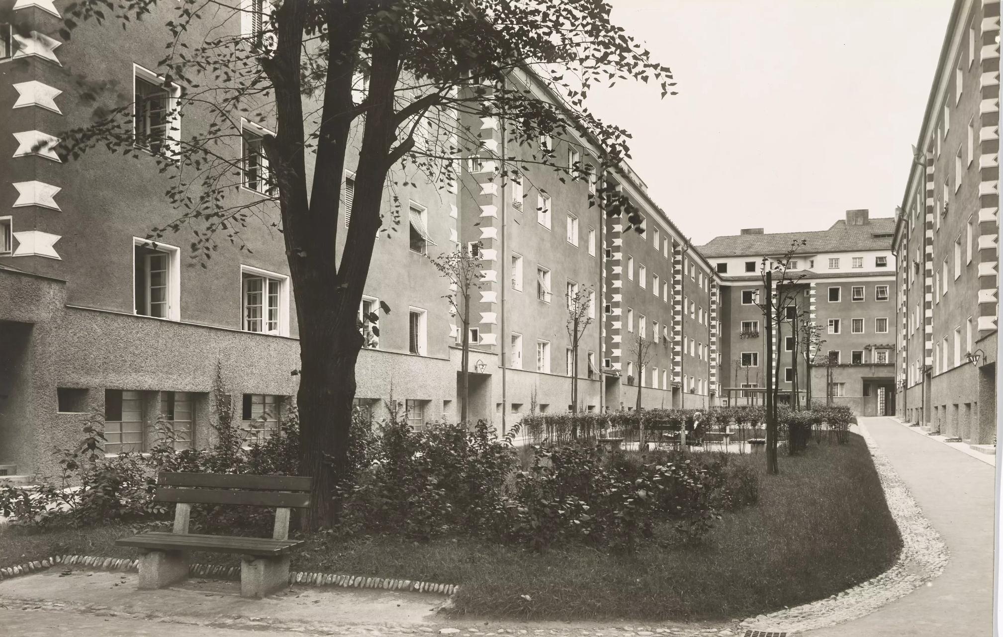 Ein Innenhof wird von fünfstöckigen Hausblöcken gesäumt. Im Hof befindet sich eine kleine Wiese mit einem Baum.  © Wien Museum, Wohnhäuser in der Penzinger Straße, Martin Gerlach, 1926. 