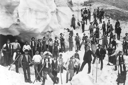 Am Fuße des Gletschers stehen mehrere Dutzend Männer mit Werkzeug in der Hand. Die meisten tragen keine Jacke, dafür haben einige Schürzen. Neben den Männern ragt die Gletschereiswand auf. © Bergbau- und Gotikmuseum Leogang, Arbeitsgruppe, 1897
