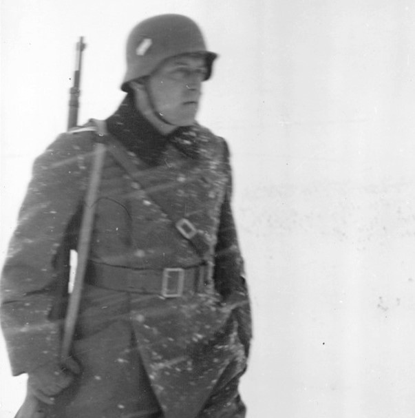 Ein Soldat in Uniform, mit Gewehr und Helm auf dem Kopf. Auf der Uniform ist Schnee und um ihn ist es weiß.   © Wikimedia