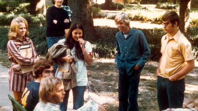 Einige Teenager stehen um eine Bank, zwei sitzen darauf. Im Hintergrund befindet sich ein Park. © Flickr, Ed Uthman, Rhodes College, 1970er. 