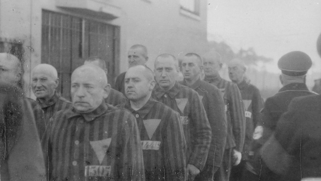 Häftlinge des KZ Sachsenhausen stehen vor einem Haus in der Reihe. Sie werden von Aufsehern bewacht. © National Archives, Heinrich Hoffmann, Häftlinge im Konzentrationslager Sachsenhausen, 1938.