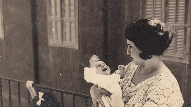 Eine Mutter mit dunklen Haaren und angespanntem Gesichtsausdruck hält ein Baby im Arm. Das Baby schreit und strampelt. Links neben der Frau ist der Kopf eines Mädchens mit weißer Schleife im Haar zu sehen.  © Wikimedia, Mutter mit Baby, 1935. 
