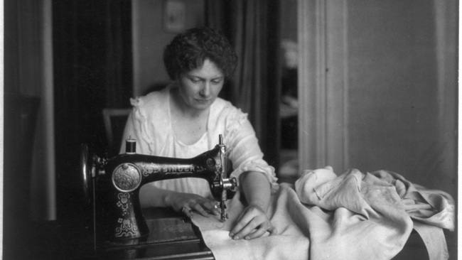 Eine Frau sitzt an einer Singer-Nähmaschine und näht.  © Wikimedia. 