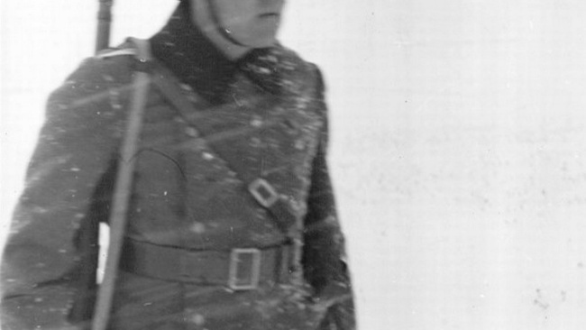 Ein Soldat in Uniform, mit Gewehr und Helm auf dem Kopf. Auf der Uniform ist Schnee und um ihn ist es weiß.   © Wikimedia