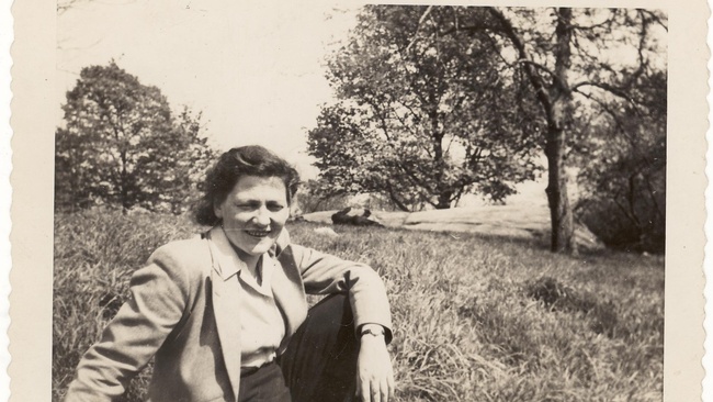 Marie Jahoda sitzt in einer hellen Jacke mit Kragen in einem Park. Sie trägt die Haare zurückgesteckt. Im Hintergrund befinden sich hohes Gras und einige Bäume.  © Archiv für die Geschichte der Soziologie in Österreich 