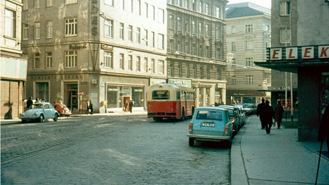 Straßenansicht in Wien mit einer kopfsteingepflasterten Straße, parkenden Autos am Straßenrand und einem Bus. Die Straße ist von mehrstöckigen Wohnhäusern gesäumt.  © Gustav Stehno, Wikimedia 