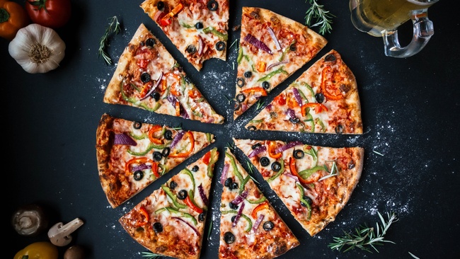 Auf dunklem Untergrund liegt eine Pizza. Belegt ist sie mit Tomatensauce und verschiedenem Gemüse.  © Wikimedia