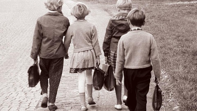 Vier Kinder gehen am Straßenrand entlang, jedes hat eine Tasche in der Hand.  © Wikimedia. 