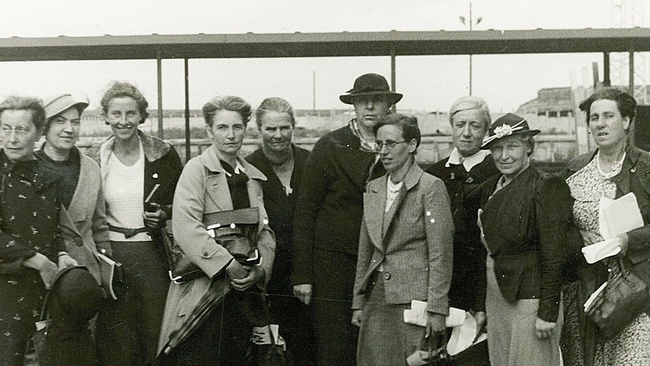 Eine Gruppe Frauen in festlicher Kleidung, einige mit Hut und Blazer, stehen nebeneinander und blicken in die Kamera. Dahinter ein Bahnsteig und eine Wiese.  © Wikimedia