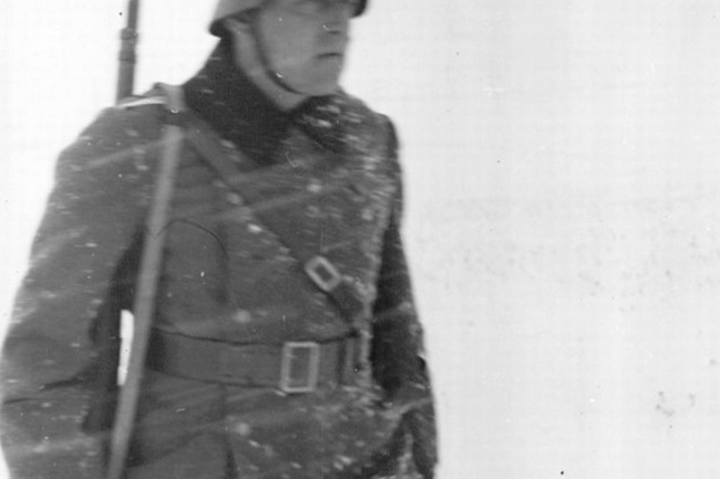 Ein Soldat in Uniform, mit Gewehr und Helm auf dem Kopf. Auf der Uniform ist Schnee und um ihn ist es weiß.   © Wikimedia
