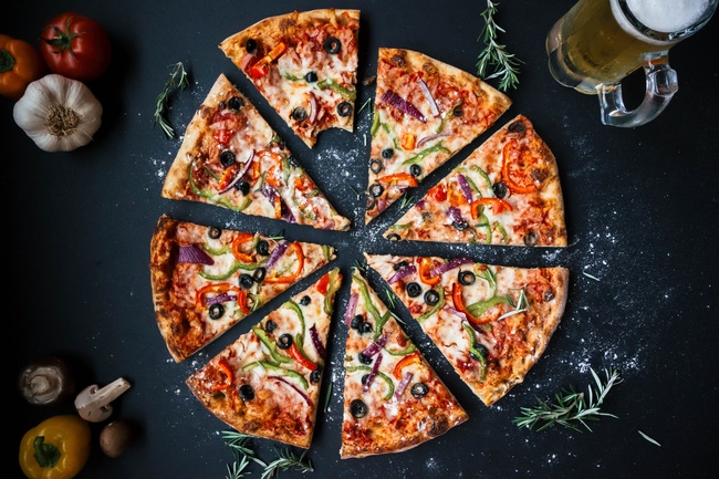 Auf dunklem Untergrund liegt eine Pizza. Belegt ist sie mit Tomatensauce und verschiedenem Gemüse.  © Wikimedia