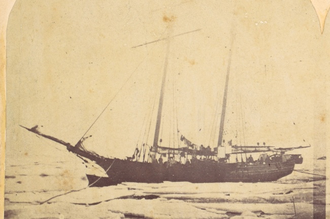 Ein zweimastiges Schiff, auf dem die Silhouetten von Menschen zu erkennen sind, ist umgeben von Eis und Schnee. © Wikipedia