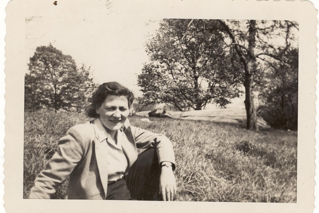 Marie Jahoda sitzt in einer hellen Jacke mit Kragen in einem Park. Sie trägt die Haare zurückgesteckt. Im Hintergrund befinden sich hohes Gras und einige Bäume.  © Archiv für die Geschichte der Soziologie in Österreich 