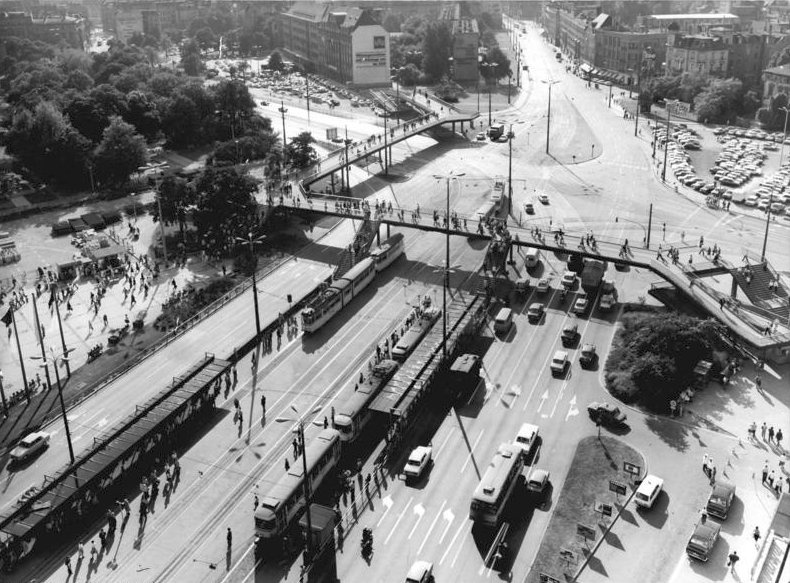 Auf einem von oben fotografierten asphaltierten Platz fahren Autos und Straßenbahnen. Über den Platz führt eine Fußgängerbrücke. Es gibt kaum Vegetation.  © Wikimedia, Waltraud Grubitzsch, Bundesarchiv, CC-BY-SA 3.0. 